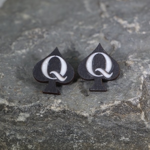 May include: A pair of black wooden earrings shaped like a spade with a white letter Q in the center.
