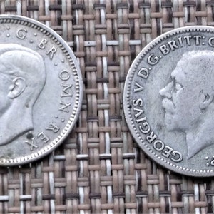 May include: Two silver British coins featuring the profile of King George VI. The obverse side of the coin features the inscription "GEORGIVS VI D.G.BRITT.OMN.REX F.D.IND.IMP." and the reverse side features the inscription "DIG.BR.OMN.REX."