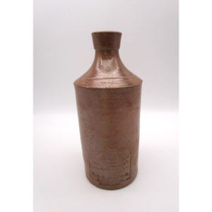 May include: A brown stoneware bottle with a cylindrical body and a narrow neck. The lower section features an embossed rectangular stamp with the text P & J ARNOLD LONDON ENGLAND. The surface has a smooth, matte finish with subtle color variations.
