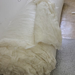 May include: A large roll of white cotton batting, a natural and organic material, is shown. The batting is rolled up tightly and is ready to be used for stuffing pillows, cushions, or other items. The label on the roll reads "I SLEEP SIMPLE Natural * Organic * Made in the USA".