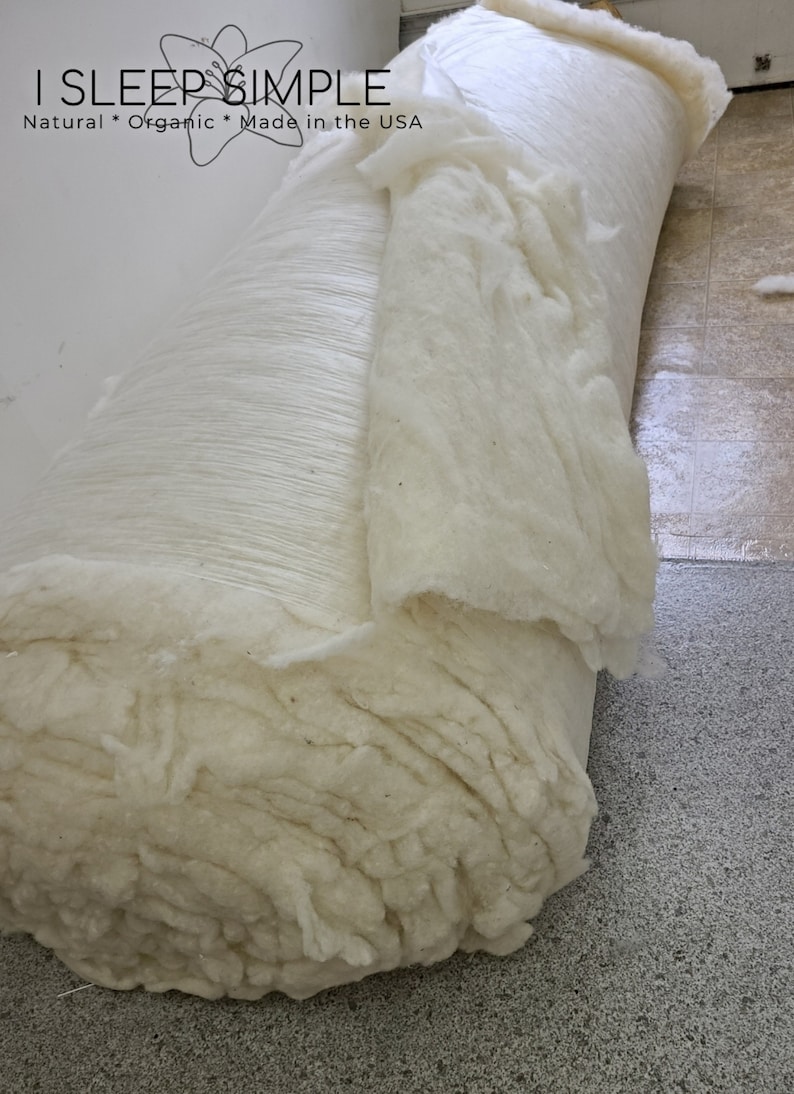 May include: A large roll of white cotton batting, a natural and organic material, is shown. The batting is rolled up tightly and is ready to be used for stuffing pillows, cushions, or other items. The label on the roll reads "I SLEEP SIMPLE Natural * Organic * Made in the USA".