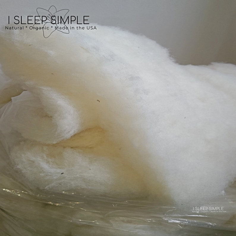 May include: A close-up of a large, white, fluffy pile of organic cotton filling. The cotton is packaged in a clear plastic bag. The text "I SLEEP SIMPLE Natural Organic Made in the USA" is visible at the top of the image.