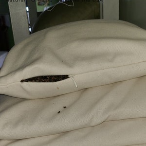 Peut inclure: Une pile de taies d'oreiller blanches avec une ouverture &agrave; glissi&egrave;re sur la taie d'oreiller sup&eacute;rieure. La fermeture &eacute;clair est ouverte et vous pouvez voir des coques de sarrasin brun &agrave; l'int&eacute;rieur. Les taies d'oreiller ont une texture subtile et sont faites de tissu naturel.