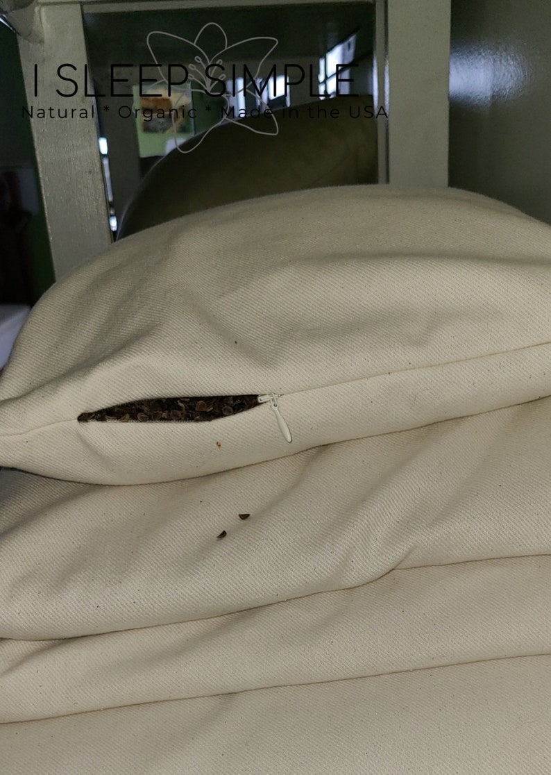 Peut inclure: Une pile de taies d'oreiller blanches avec une ouverture &agrave; glissi&egrave;re sur la taie d'oreiller sup&eacute;rieure. La fermeture &eacute;clair est ouverte et vous pouvez voir des coques de sarrasin brun &agrave; l'int&eacute;rieur. Les taies d'oreiller ont une texture subtile et sont faites de tissu naturel.