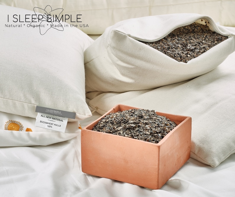 Peut inclure: Un oreiller en coton blanc rempli de coques de sarrasin. L'oreiller est ouvert, r&eacute;v&eacute;lant les coques de sarrasin &agrave; l'int&eacute;rieur. L'oreiller est pos&eacute; sur un drap blanc. Le texte "I SLEEP SIMPLE" est imprim&eacute; sur l'oreiller. Le texte "ALL NEW MATERIAL BUCKWHEAT HULLS 100%" est imprim&eacute; sur une &eacute;tiquette attach&eacute;e &agrave; l'oreiller.