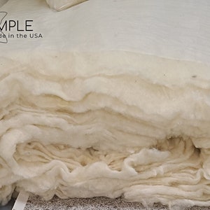 May include: A close-up of a large roll of white cotton batting. The batting is folded and stacked, creating a soft and fluffy texture. The label "I SLEEP SIMPLE Natural * Organic * Made in the USA" is visible on the top of the roll.