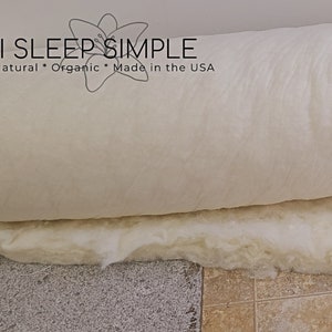 May include: A white, rolled-up, organic cotton mattress topper with the text "I SLEEP SIMPLE Natural * Organic * Made in the USA" printed on the top.