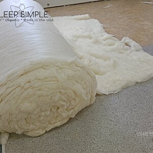 May include: A close-up of a large roll of white cotton batting, unfurled on a gray carpet. The roll is labeled "I SLEEP SIMPLE Natural * Organic * Made in the USA".