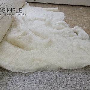 May include: A roll of white cotton batting is unfurling on a gray carpet. The batting is labeled "I SLEEP SIMPLE Natural * Organic * Made in the USA".