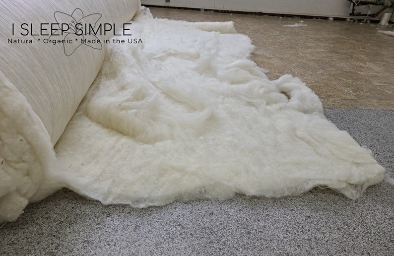 May include: A roll of white cotton batting is unfurling on a gray carpet. The batting is labeled "I SLEEP SIMPLE Natural * Organic * Made in the USA".