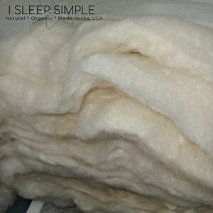 May include: A close-up of a stack of white, fluffy, natural wool batting. The wool is soft and airy, and it is perfect for stuffing pillows, cushions, and other home decor items. The label on the top of the stack reads "I Sleep Simple Natural * Organic * Made in the USA".
