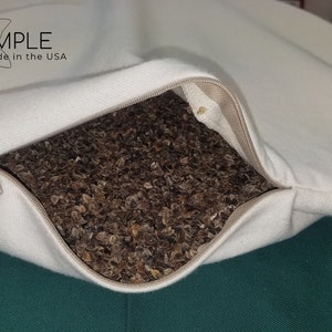 Peut inclure: Une taie d'oreiller blanche avec une fermeture &eacute;clair ouverte, r&eacute;v&eacute;lant un oreiller en coque de sarrasin &agrave; l'int&eacute;rieur. La taie d'oreiller porte l'inscription "I SLEEP SIMPLE. Natural * Organic * Made in the USA".