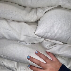 Peut inclure: Une pile d'oreillers en coton biologique blanc avec une main pos&eacute;e dessus. Les oreillers sont fabriqu&eacute;s par I Sleep Simple, Naturel Biologique, Fabriqu&eacute; aux &Eacute;tats-Unis.