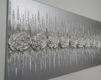 May include: Silver abstract canvas art with fabric-like flowers and vertical glitter accents. The artwork has a modern, elegant aesthetic, with a monochromatic colour scheme. The flowers are arranged in a row across the canvas.