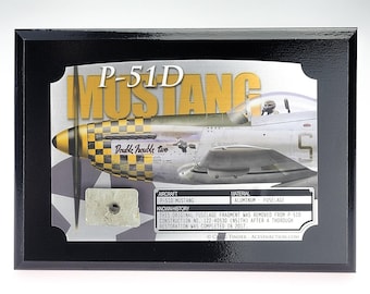 Könnte beinhalten: Eine rechteckige schwarze Holzplakette mit einer Illustration eines P-51D Mustang Flugzeugs mit gelb-schwarz karierter Nase. Der Text lautet P-51D MUSTANG und Double Trouble Two. Ein kleines Rumpffragment aus Metall ist auf dem Display befestigt.