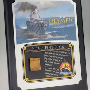 May include: A black framed display plaque featuring a painting of the HMT Olympic ship with dazzle camouflage. Below the painting, a rectangular section contains text about the Pitch Pine Deck and a small, square piece of light brown wood.