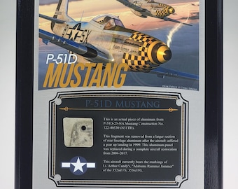 Könnte beinhalten: Eine rechteckige schwarze Plakette mit einer Illustration von zwei P-51D Mustang Flugzeugen im Flug. Die Plakette enthält den Text P-51D MUSTANG und ein kleines, quadratisches Stück Aluminium aus dem Flugzeug mit einer Beschreibung.