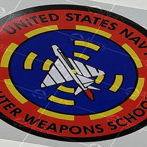 Puede incluir: Adhesivo circular con las palabras "UNITED STATES NAVY FIGHTER WEAPONS SCHOOL" en texto rojo. El centro tiene un círculo azul con un avión blanco y un diseño amarillo y azul.