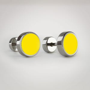 Puede incluir: Dos pendientes de botón de acero inoxidable con centros circulares de color amarillo brillante. Los pendientes tienen un acabado metálico pulido y un diseño sencillo y moderno. Los centros amarillos proporcionan un toque de color.