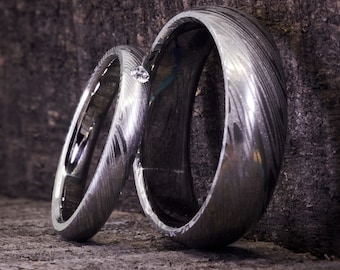 May include: Two silver wedding bands with a textured, patterned finish. The bands are stacked on top of each other, with a small diamond visible between them.