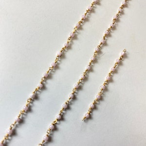 May include: Three strands of pink and gold bead chains of varying lengths. The chains are made of small, round, pink beads strung on a gold wire.