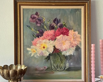 May include: A framed oil painting of a bouquet of pink, white, and purple flowers in a green vase. The painting is set on a table with a gold bowl and books.