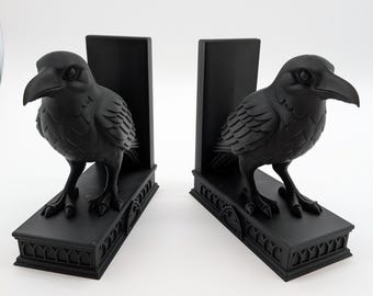 May include: Two black raven bookends. Each bookend has a detailed raven sculpture on a rectangular base with decorative trim. The ravens face outwards, with their beaks slightly open.