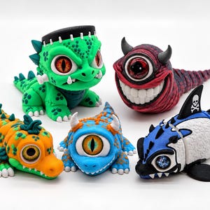 May include: A collection of five articulated monster figurines. One is a green creature with stitches, one is a red cyclops with horns, one is an orange and green lizard-like creature, one is a blue cyclops, and one is a blue and white shark-like figure.