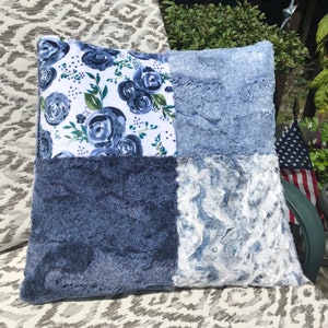 May include: A blue and white patchwork pillow with a floral pattern on one side. The pillow is made of soft, plush fabric and is perfect for adding a touch of comfort and style to any room.
