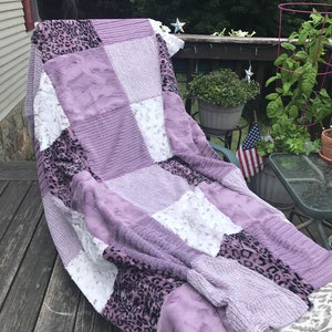 May include: A patchwork quilt with a variety of textures and patterns, including a purple, white, and black leopard print. The quilt is made of soft, plush fabric and is perfect for cuddling up on the couch.