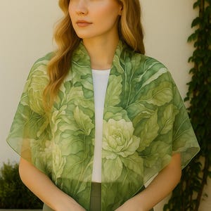 May include: A green silk scarf with a floral pattern. The scarf is draped around a person's neck and shoulders.
