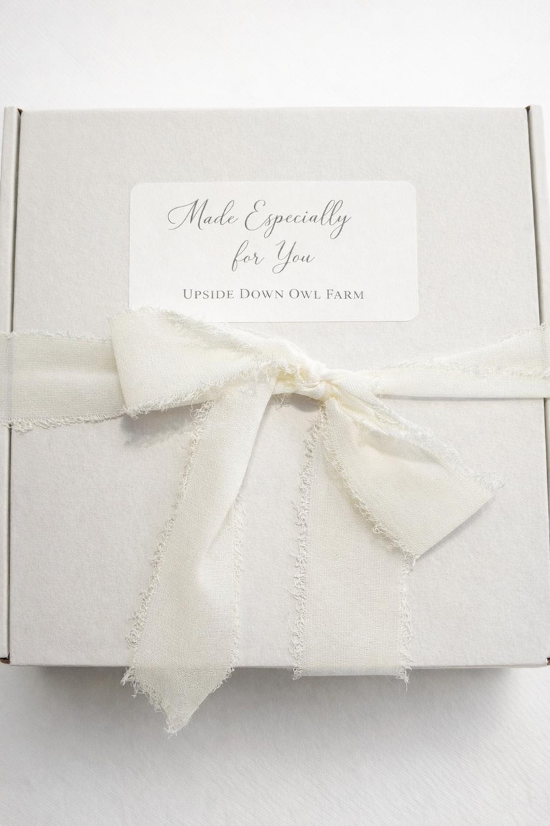 K&ouml;nnte beinhalten: Eine wei&szlig;e Geschenkbox, gebunden mit einem cremefarbenen Band und einer Schleife. Die Box hat ein Etikett mit der Aufschrift "Made Especially for You" und "Upside Down Owl Farm". Das Band hat ausgefranste Kanten.