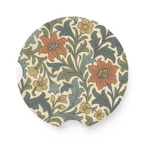 May include: Round car coaster with a floral pattern. The design features orange, yellow, and blue flowers with green leaves on a cream background. The coaster has a small notch on one side.