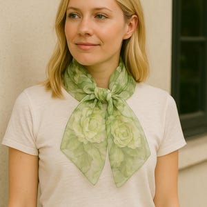 May include: A woman wearing a white t-shirt and a green floral scarf tied around her neck. The scarf has a light green background with a floral pattern of white roses.
