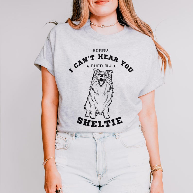 Peut inclure: T-shirt gris avec une illustration noir et blanc d'un chien Shetland. Le texte sur le t-shirt est "D&eacute;sol&eacute;, je ne t'entends pas &agrave; cause de mon Shetland."