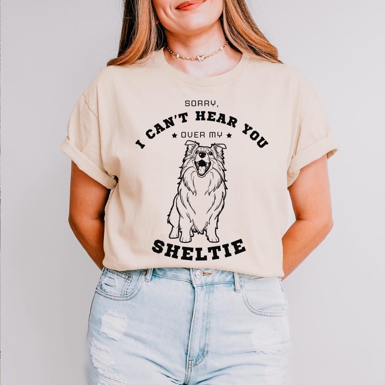 Peut inclure: Un t-shirt beige avec un graphique noir d'un chien Sheltie et le texte "D&eacute;sol&eacute;, je ne peux pas t'entendre par-dessus mon Sheltie".