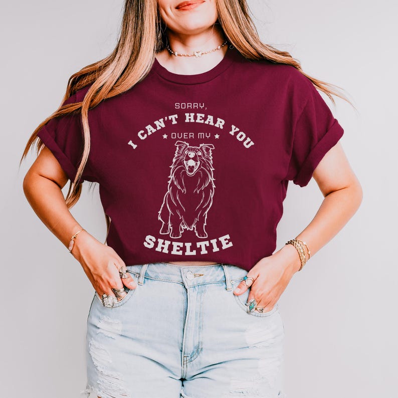 Peut inclure: Un t-shirt bordeaux avec un graphique blanc d'un chien Shetland et le texte "D&eacute;sol&eacute;, je ne t'entends pas &agrave; cause de mon Shetland".