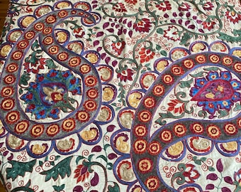 May include: A white tablecloth with intricate embroidery in shades of red, blue, green, and gold. The design features paisley patterns and floral motifs.