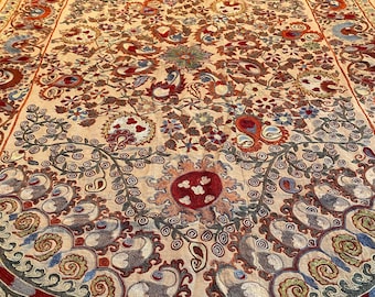 May include: A large, cream-colored rug with intricate embroidery in shades of red, blue, and green. The design features paisley patterns, floral motifs, and swirling vines.