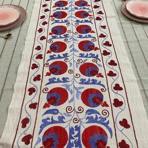 Può includere: Tovaglia da tavolo in lino bianco con melograni e motivi floreali ricamati in rosso e blu.