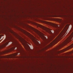 May include: A close-up of a dark red ceramic glaze with a subtle, swirling pattern. The glaze has a glossy finish and a slightly textured surface.