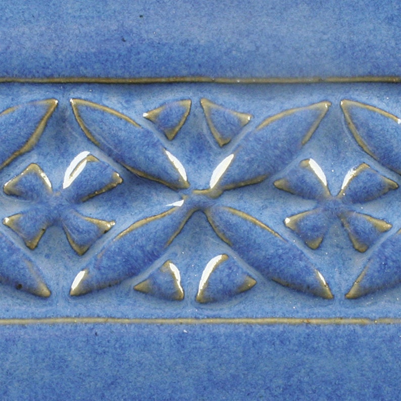 May include: A close-up of a blue ceramic tile with a raised pattern of overlapping leaves in a light brown glaze.