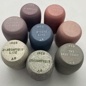 May include: A collection of eight cylindrical objects in various colors, including purple, blue, pink, and gray. Each object has a rounded top with text such as "Aubergine" and "Dragonfruit Lite". The objects are labeled with the brand "IMCO".