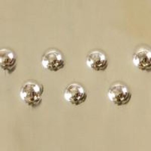 Pu&ograve; includere: Sei borchie a cupola in metallo color argento, disposte in uno schema sfalsato.