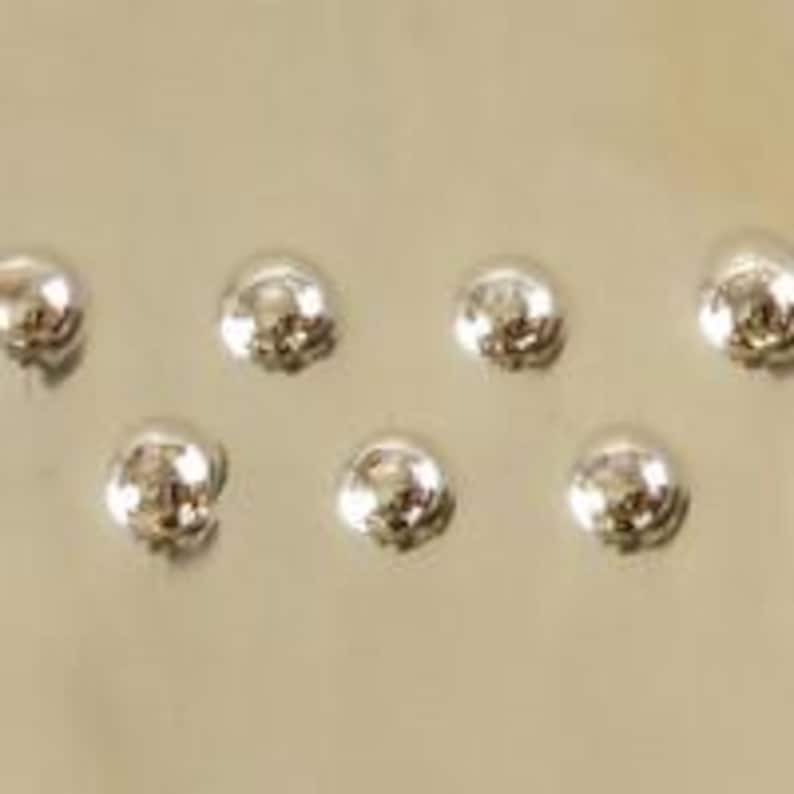 Pu&ograve; includere: Sei borchie a cupola in metallo color argento, disposte in uno schema sfalsato.