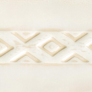 May include: A close-up of a white ceramic tile with a raised pattern of beige diamonds and triangles.