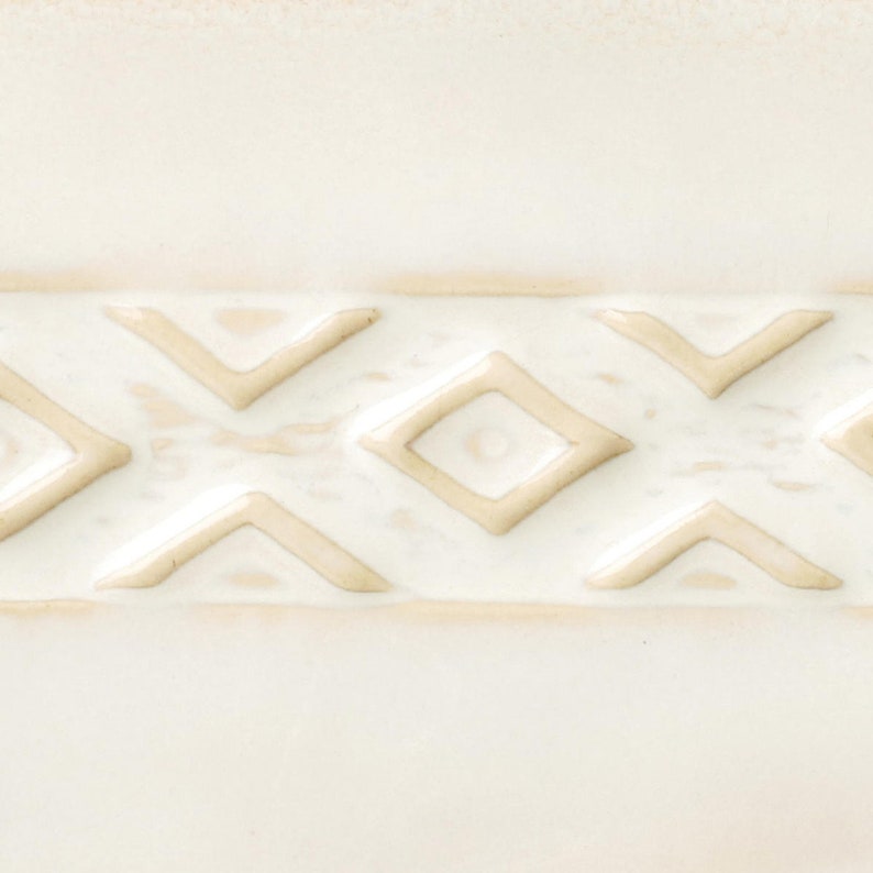 May include: A close-up of a white ceramic tile with a raised pattern of beige diamonds and triangles.