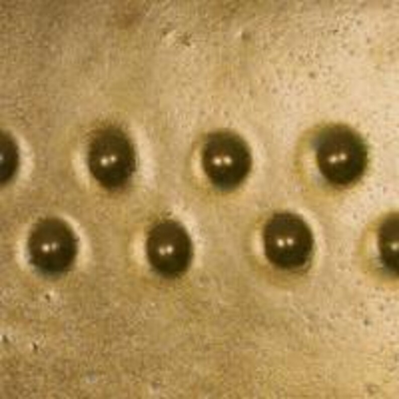 Pu&ograve; includere: Primo piano di una superficie metallica dorata con nove rientranze circolari equidistanti. Ogni rientranza contiene una piccola perla metallica rotonda.