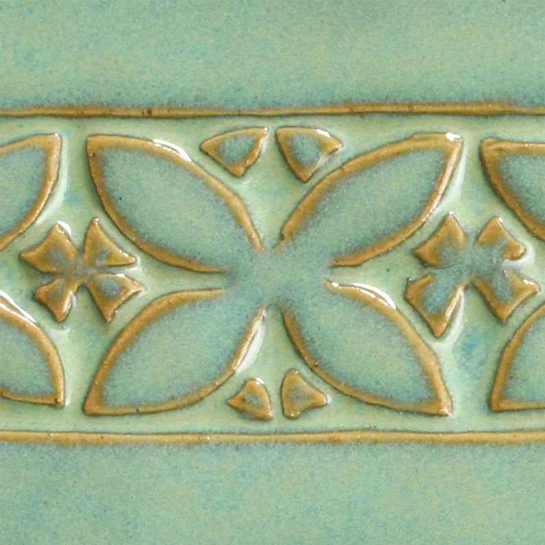 May include: A close-up of a light green ceramic tile with a raised pattern of brown flowers and leaves.