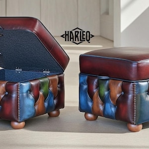 以下が含まれることがあります： 青、緑、茶色、赤の色合いのパッチワークデザインが特徴の、革製のオットマン2つ。1つは蓋が開いています。上面は濃いバーガンディ色で、ベースは小さく丸みを帯びた木製の脚で支えられています。「HARLEQ」のブランド名が見えます。